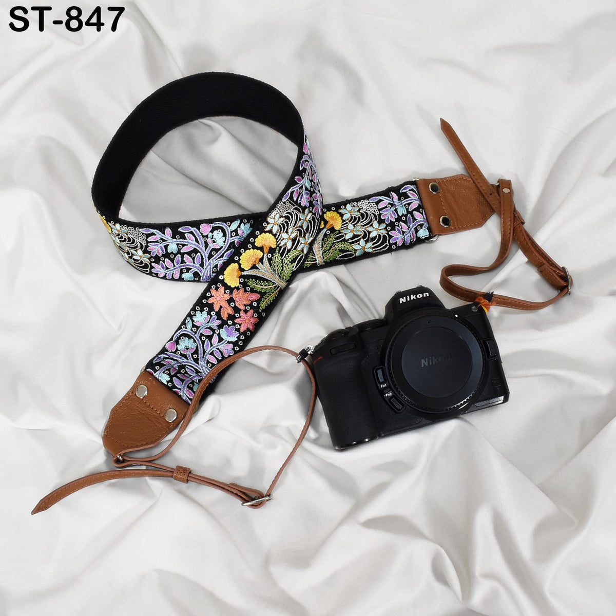 A floral patterned camera strap and a black Nikon camera are placed on a white fabric surface.