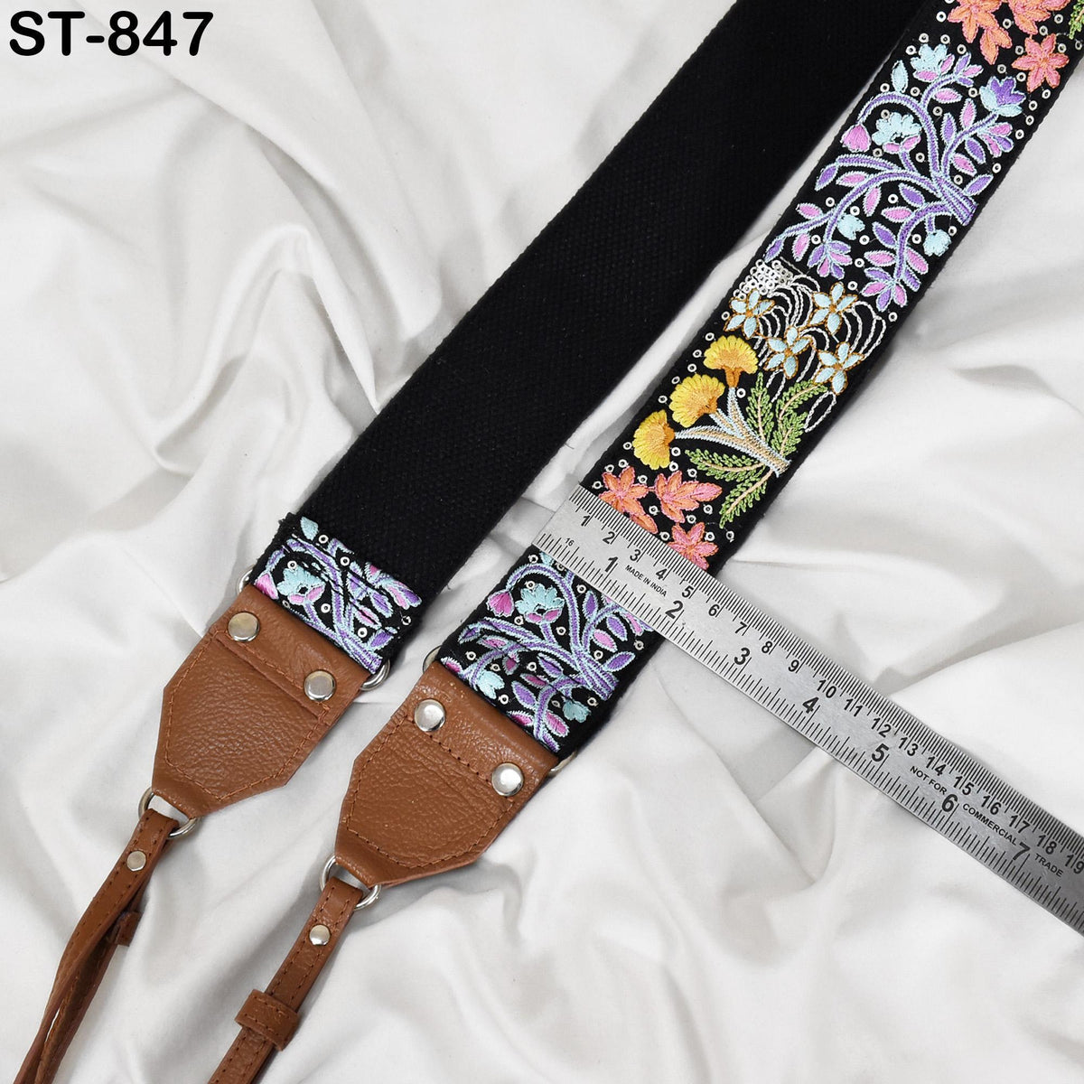 A black strap with a floral pattern and a brown leather strap are placed on a white fabric surface, with a ruler for scale.
