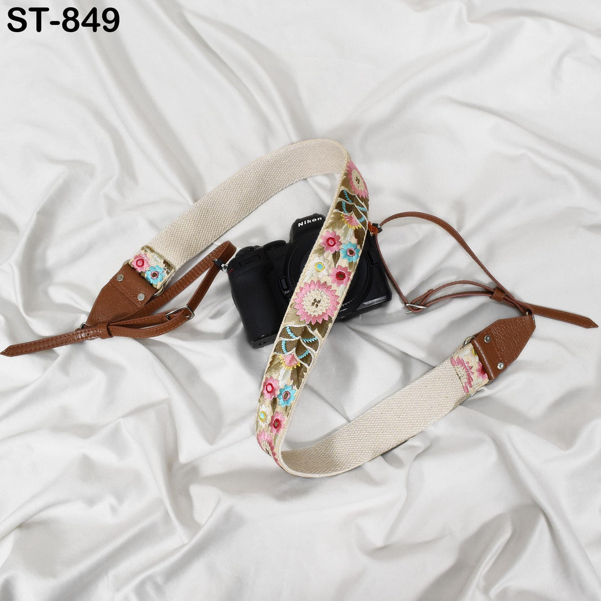 A camera strap with a floral pattern is placed on a white fabric surface.