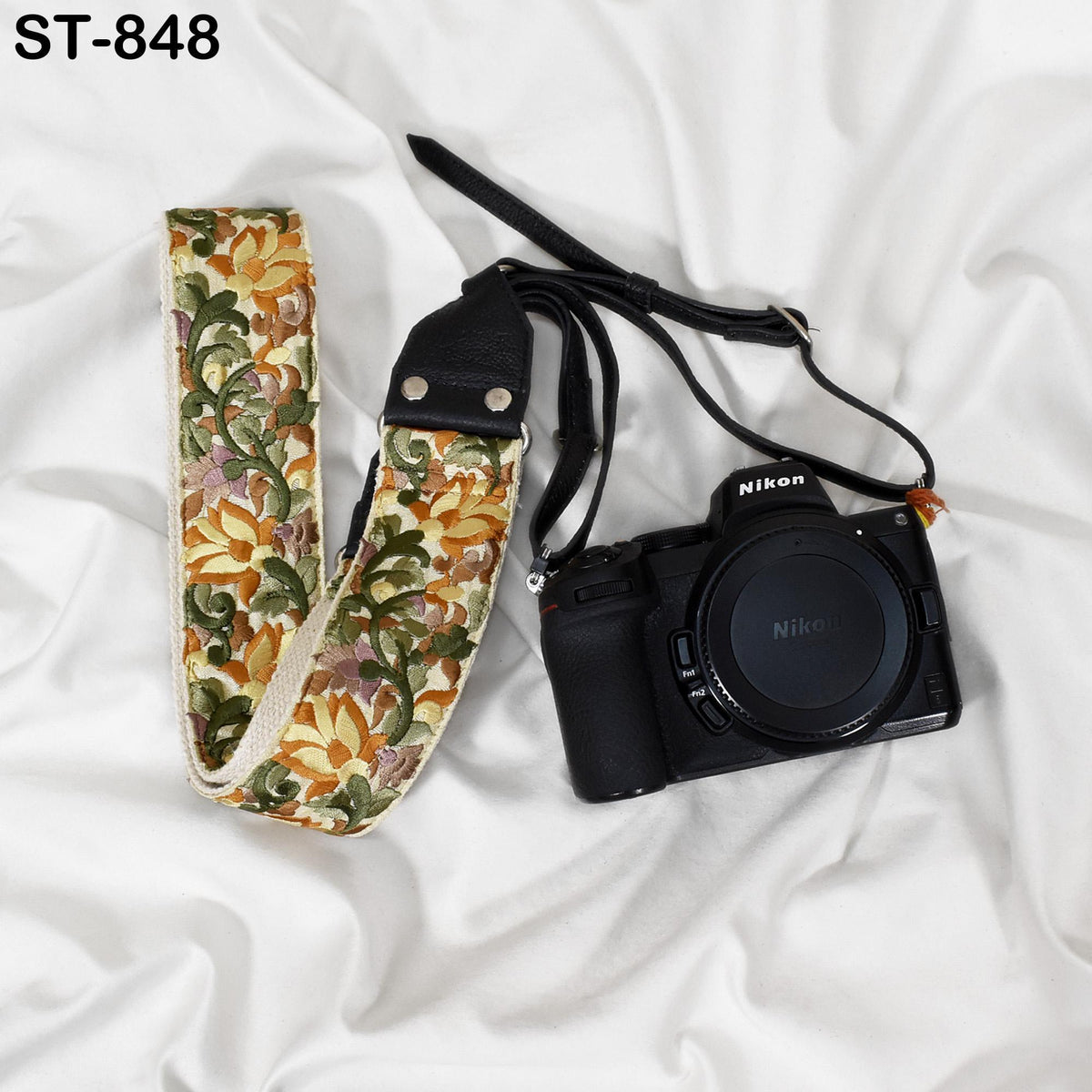 A black camera with a floral patterned strap is placed on a white surface.