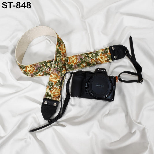 A floral patterned camera strap and a Nikon camera are placed on a white surface.