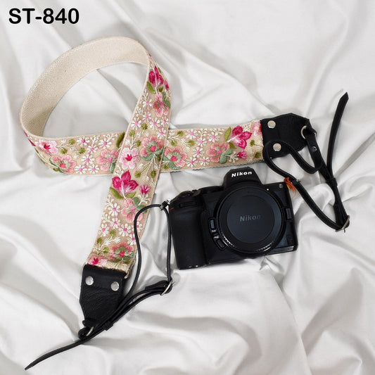 A floral patterned camera strap and a Nikon camera are placed on a white fabric surface.