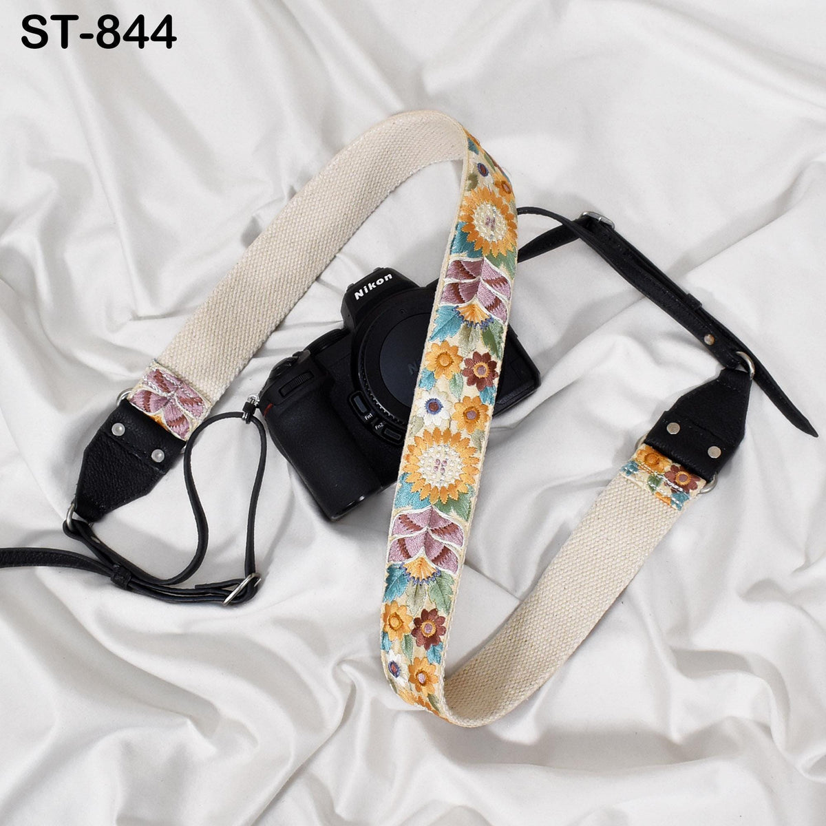 A black camera with a colorful floral patterned strap is placed on a white surface.