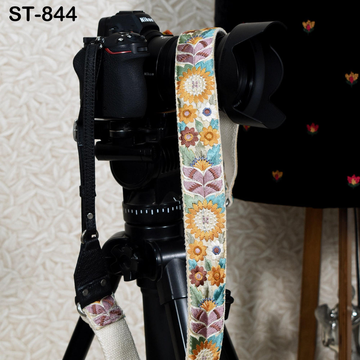 A black camera with a colorful floral patterned strap attached to it, placed on a tripod.