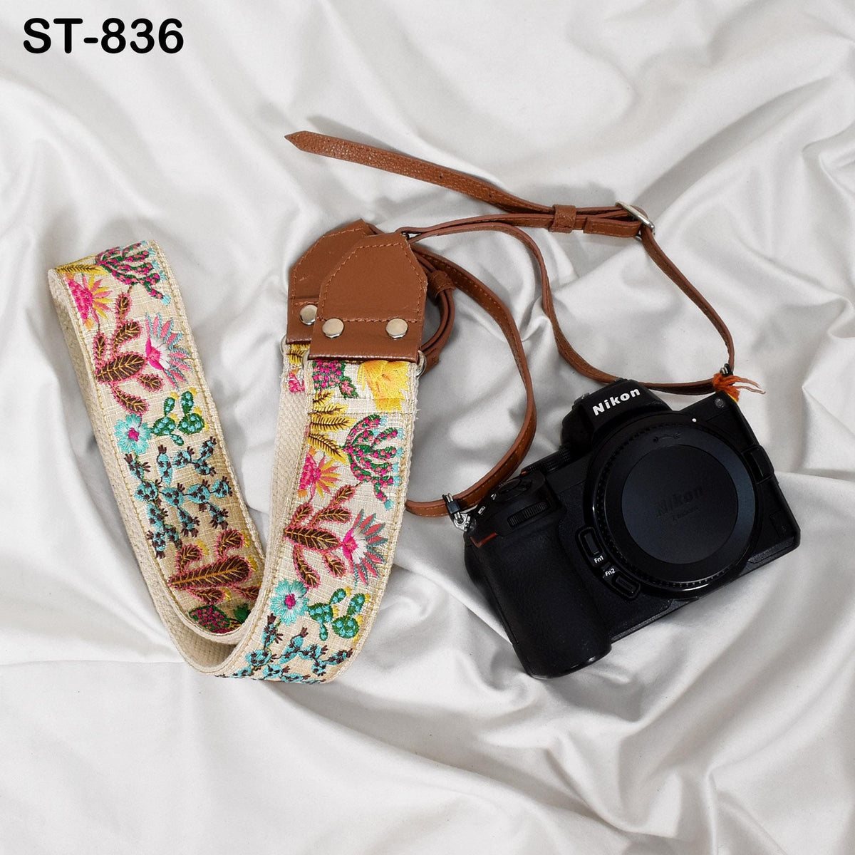 A floral patterned camera strap and a black Nikon camera are placed on a white fabric surface.