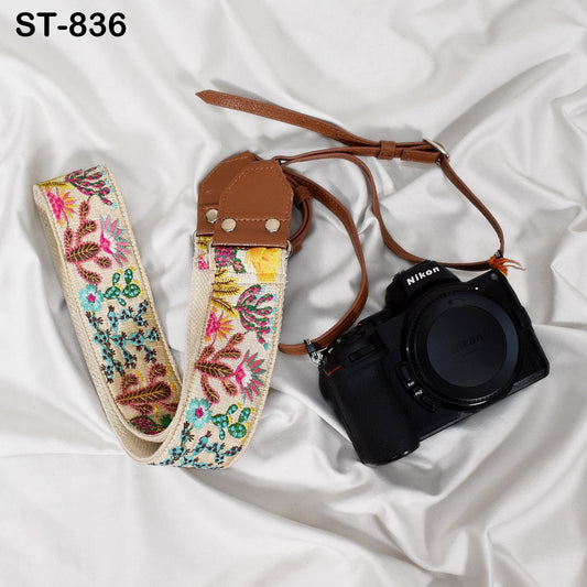 A floral patterned camera strap and a black Nikon camera are placed on a white fabric surface.
