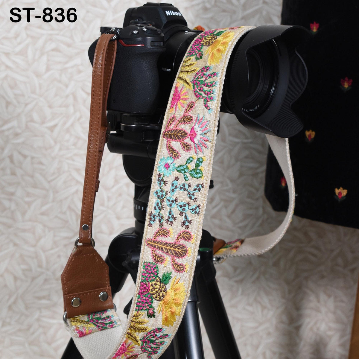 A camera strap with a floral pattern is attached to a camera, and the strap is hanging on a tripod.