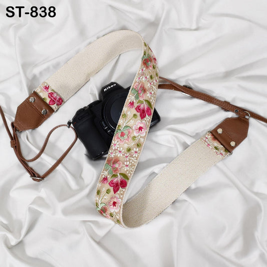 A floral patterned camera strap is draped over a black camera, with a white background.
