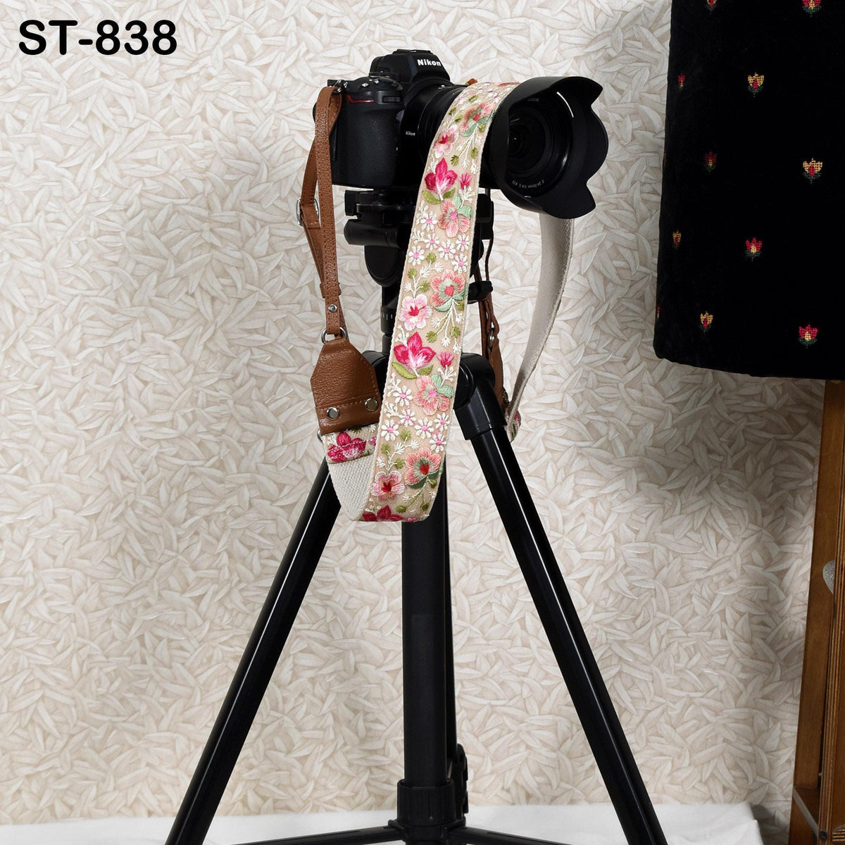 A camera mounted on a tripod, with a floral patterned strap attached to it.