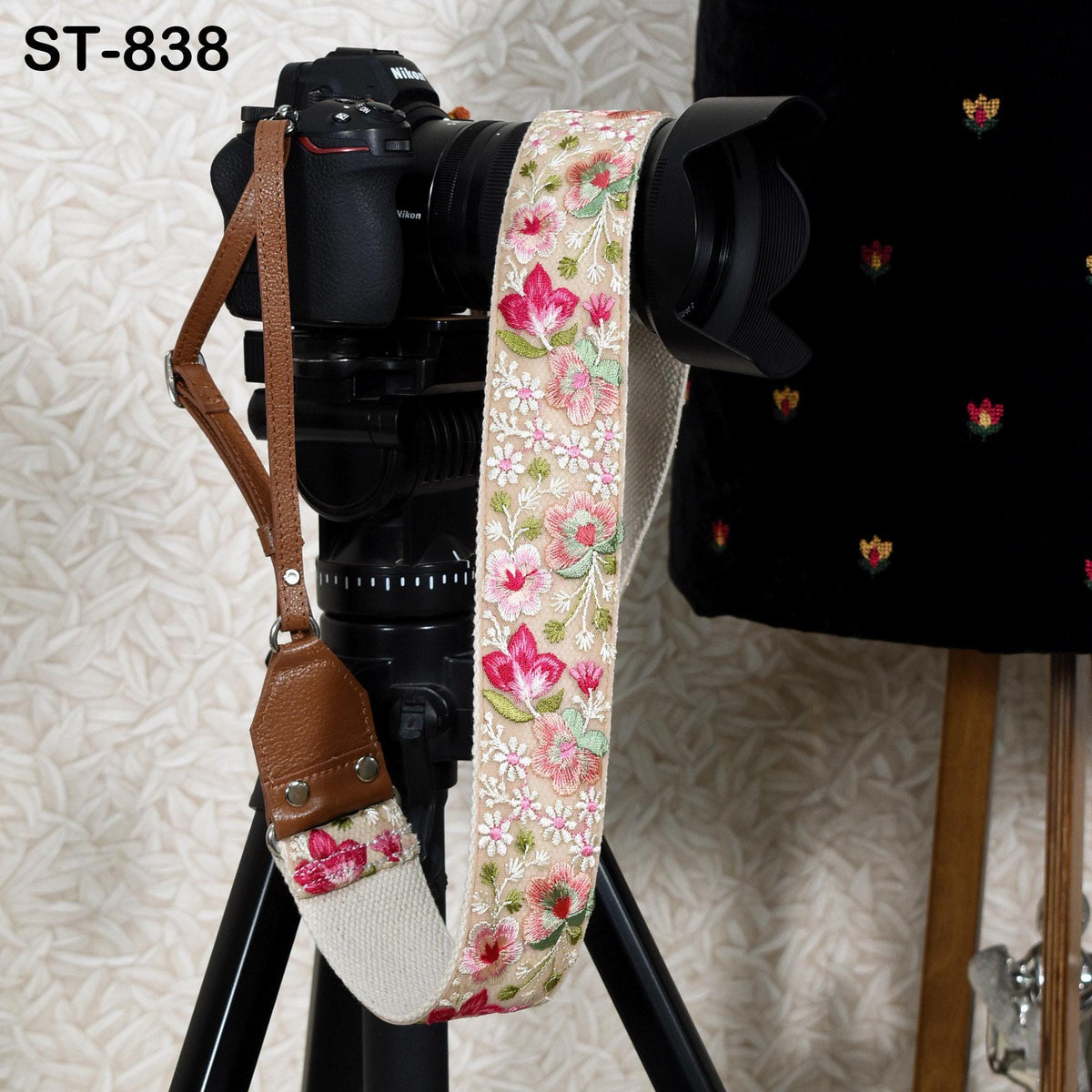 A floral patterned camera strap is attached to a black tripod, with a camera lens attached to the top of the tripod.