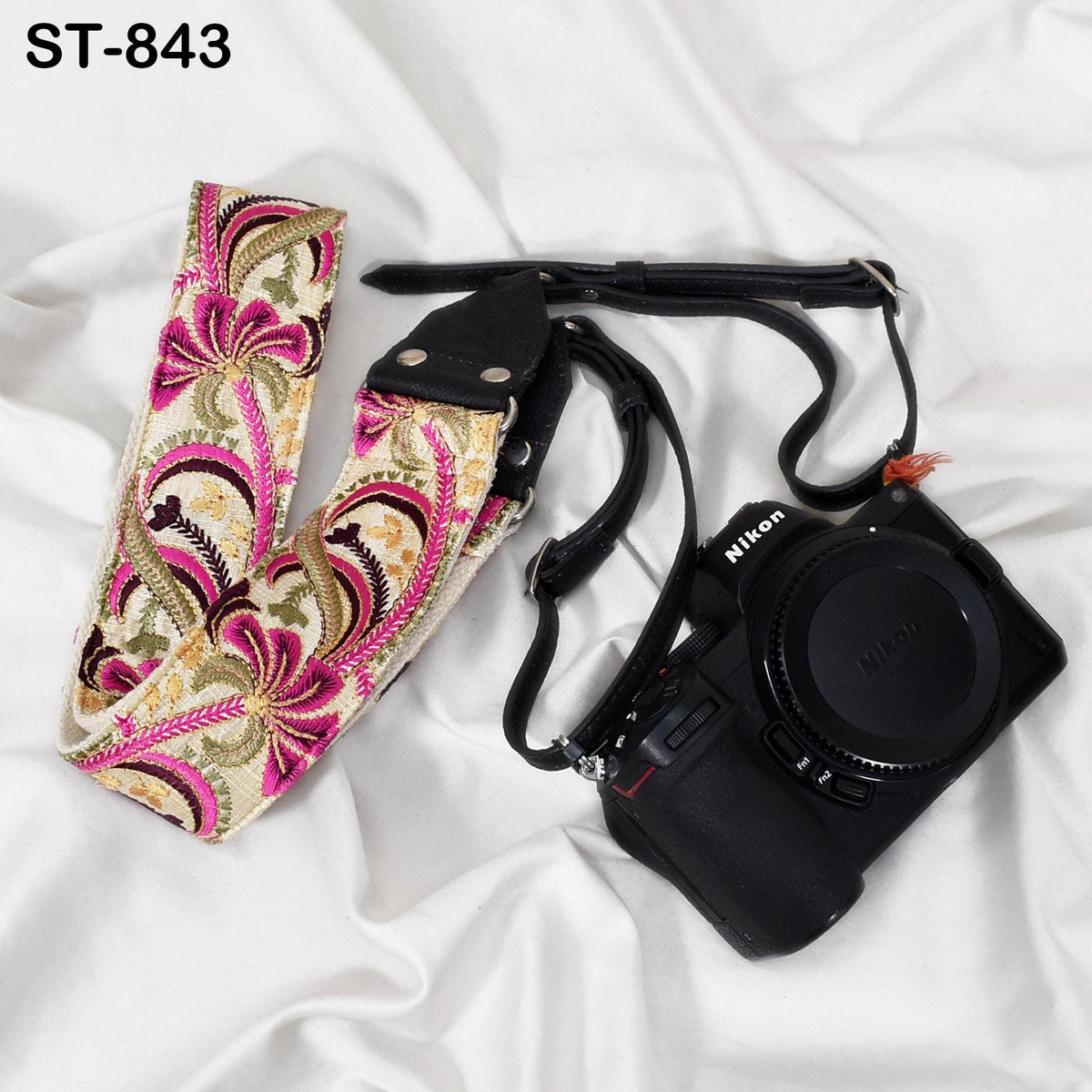 A floral patterned camera strap and a black Nikon camera are placed on a white surface.