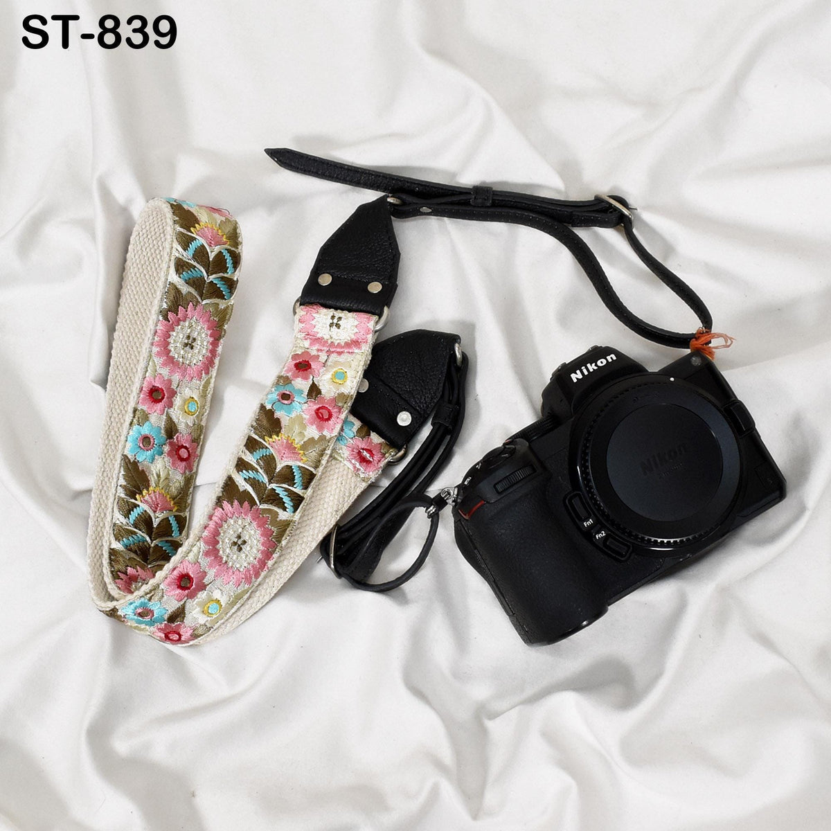 A floral patterned camera strap and a black camera body are placed on a white surface.