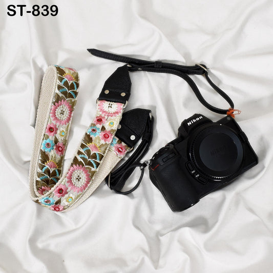 A floral patterned camera strap and a black camera body are placed on a white surface.