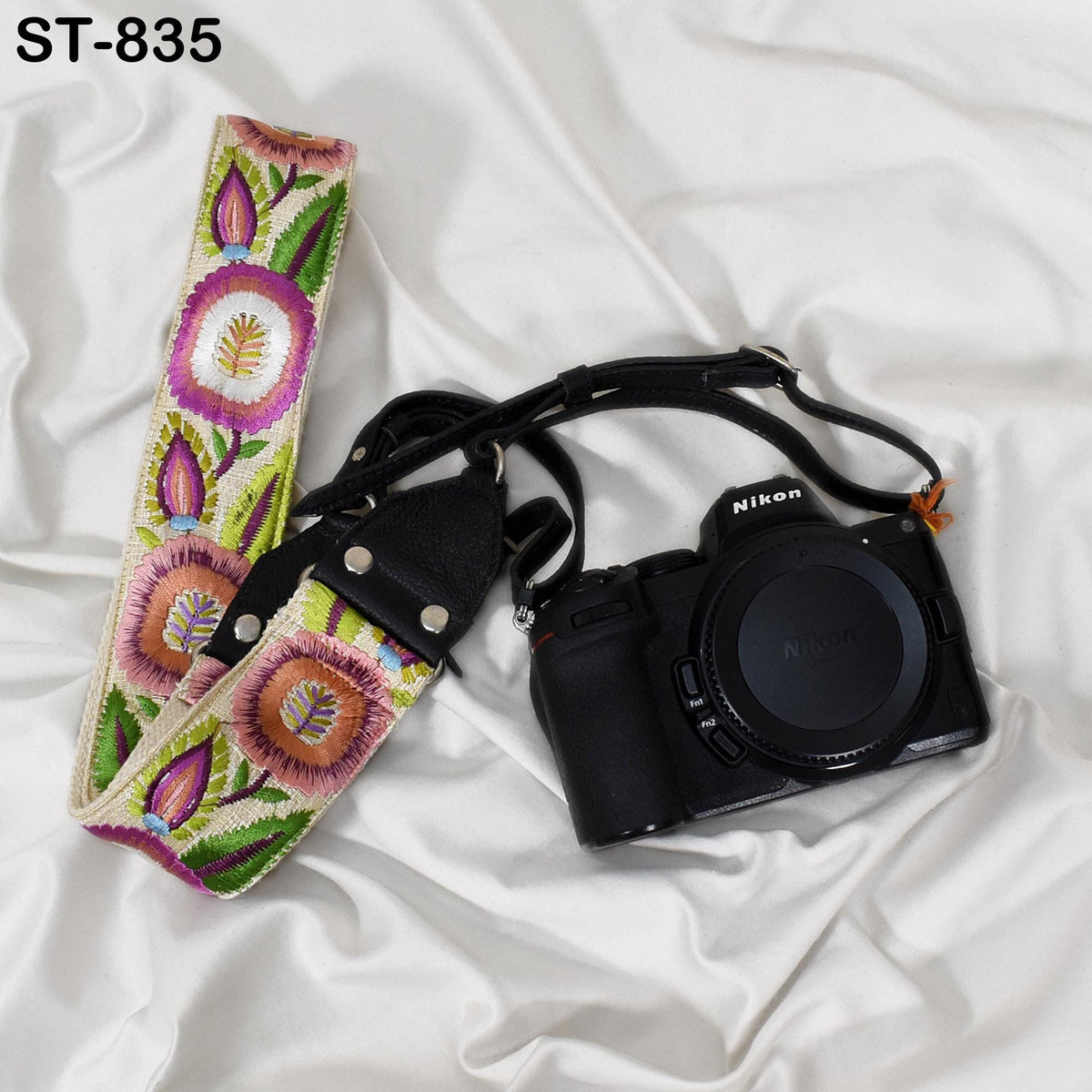 A black Nikon camera and a colorful floral patterned camera strap are placed on a white surface.