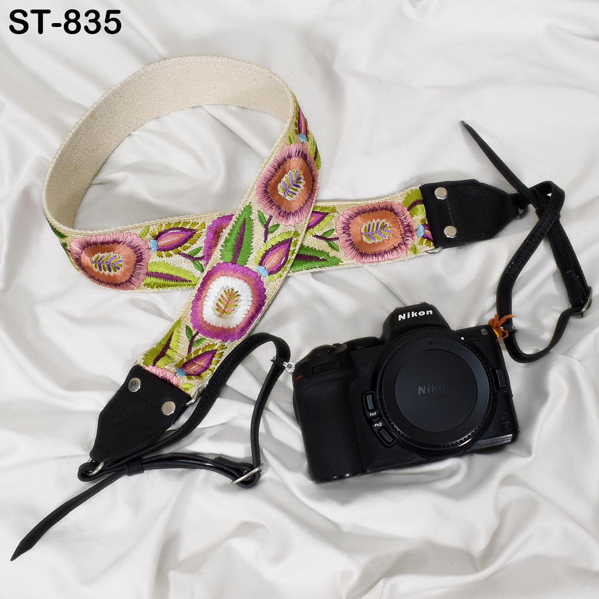 A floral patterned camera strap and a black Nikon camera are placed on a white surface.