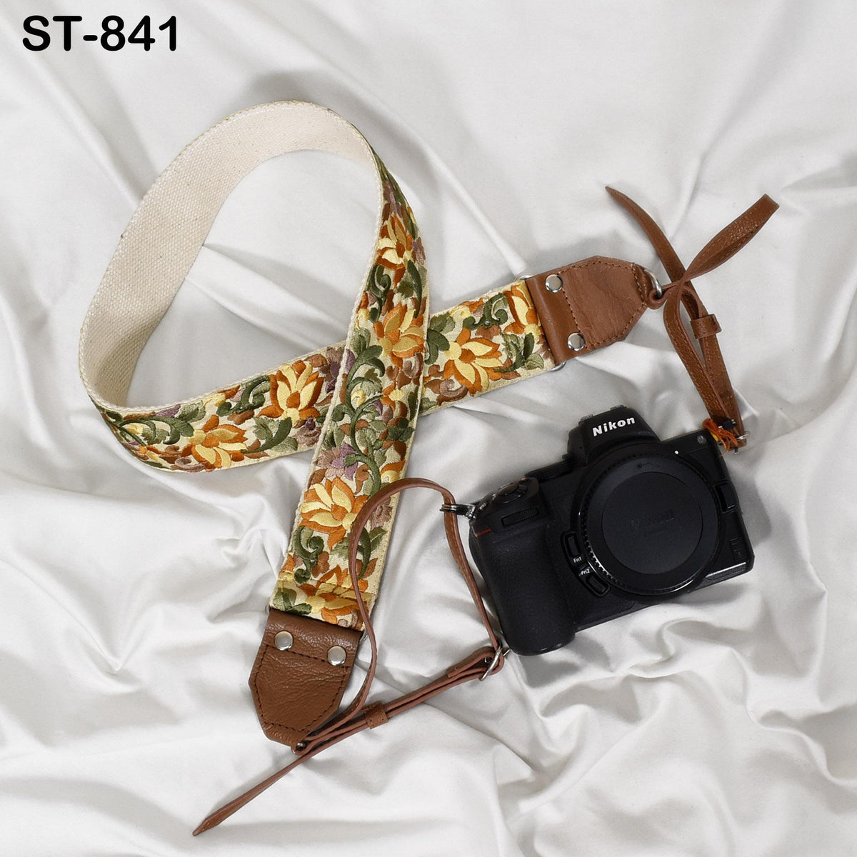 A floral-patterned camera strap and a black Nikon camera are placed on a white surface.
