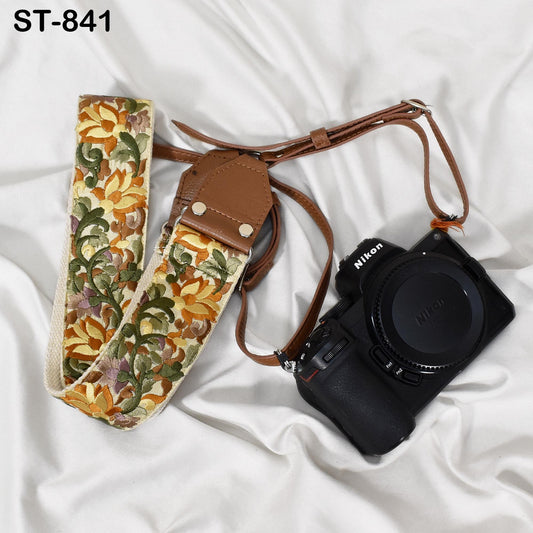 A floral patterned camera strap and a black Nikon camera are placed on a white surface.