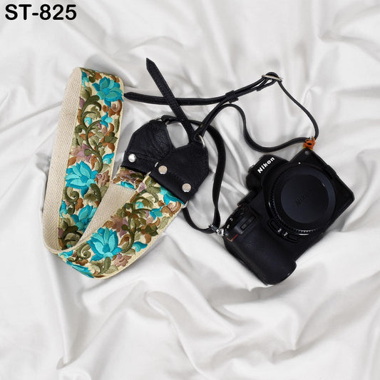 A floral patterned camera strap and a black Nikon camera are placed on a white surface.