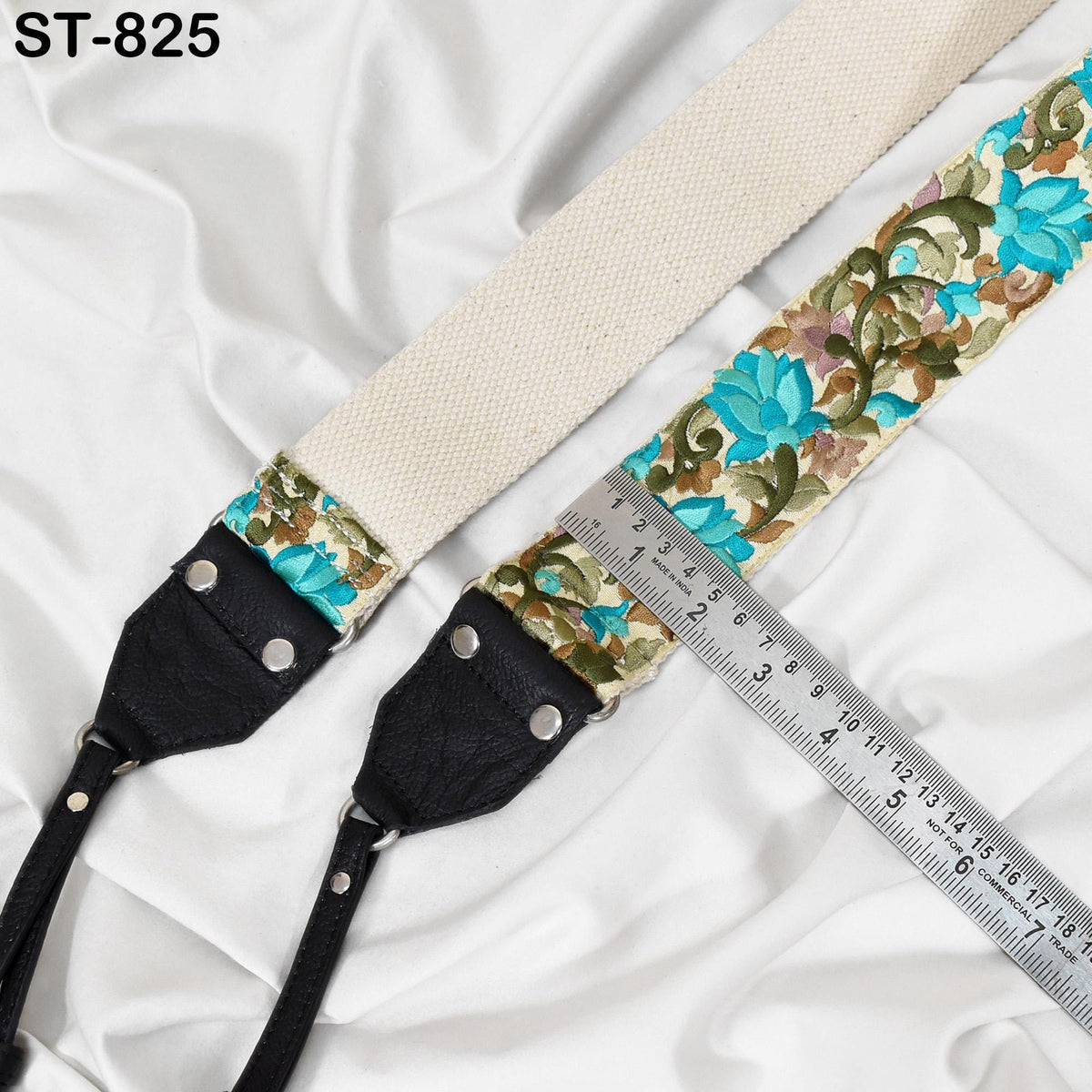 A beige strap with a floral pattern and a black leather strap are placed on a white fabric surface, with a ruler placed next to them.