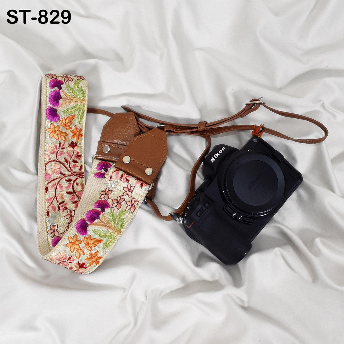 A floral patterned camera strap and a black Nikon camera are placed on a white fabric surface.