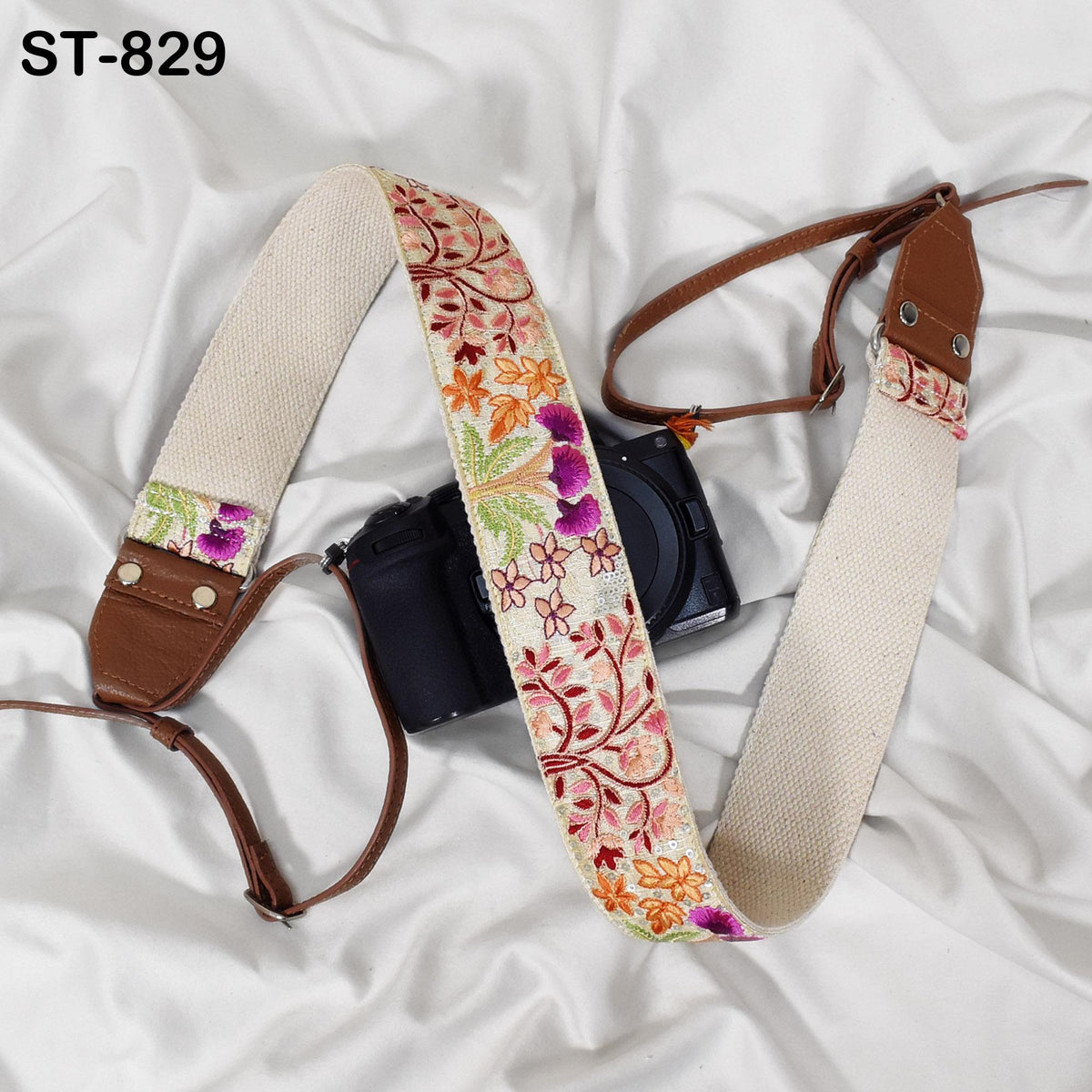 A camera strap with a floral pattern is draped over a camera, resting on a white fabric surface.