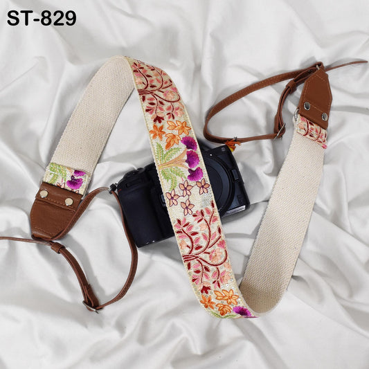 A camera strap with a floral pattern is draped over a camera, resting on a white fabric surface.