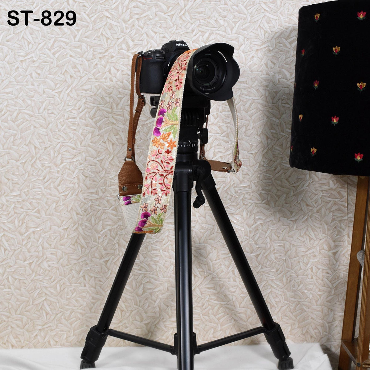 A black tripod with a camera attached to it, standing on a white surface against a patterned wall.
