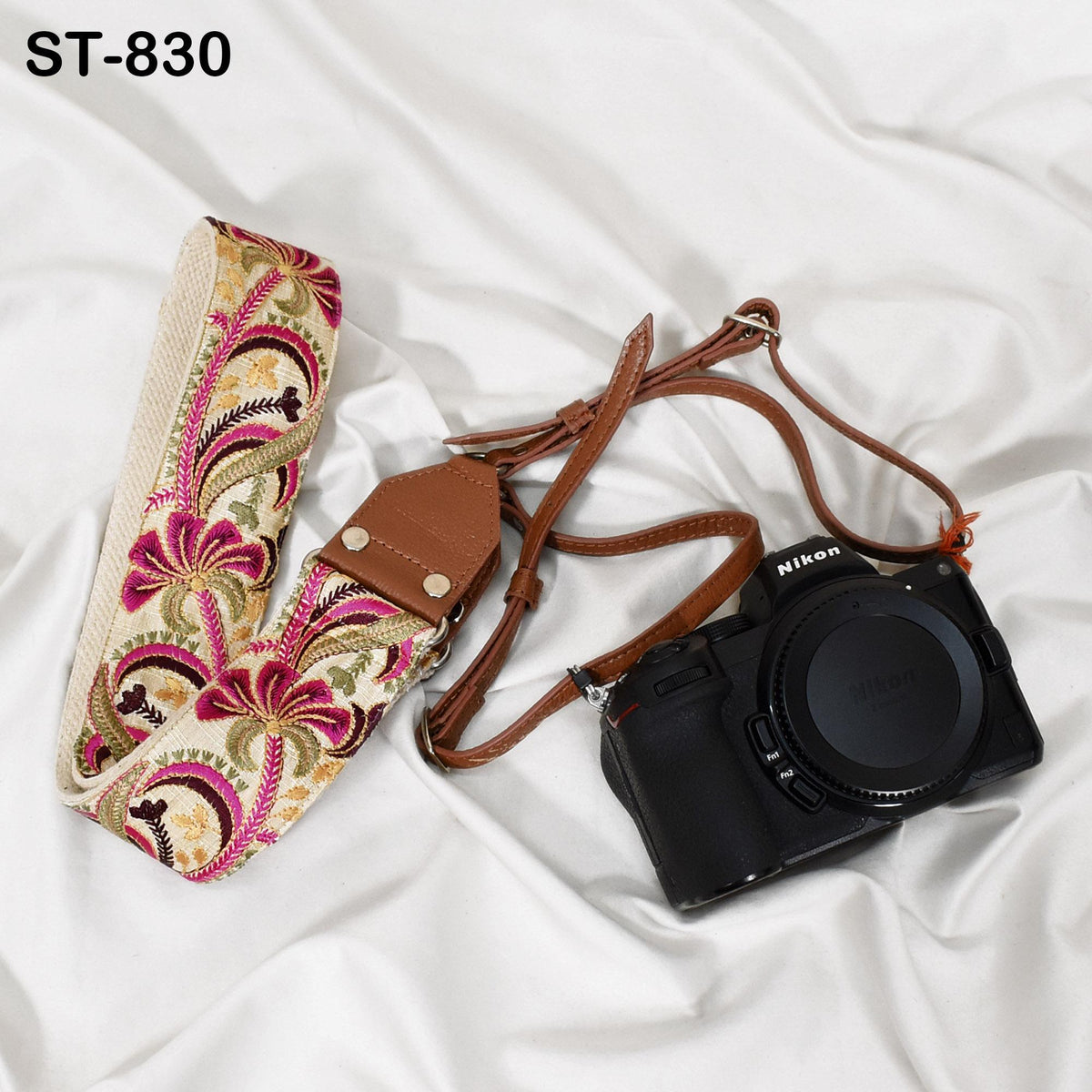 A floral patterned camera strap and a black Nikon camera are placed on a white fabric surface.