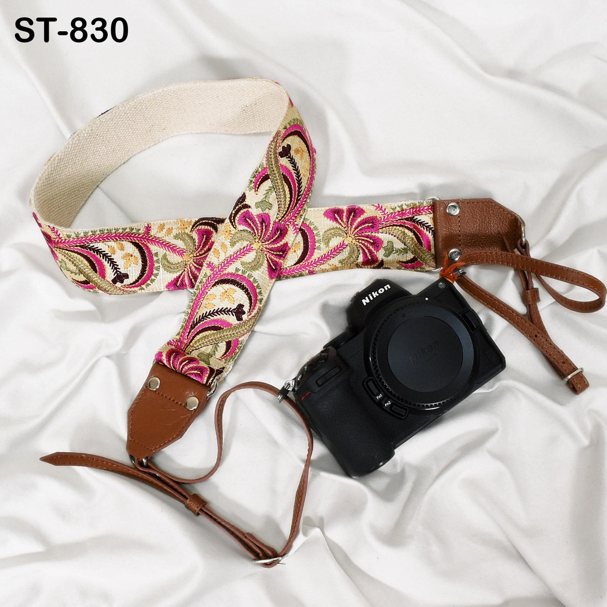 A floral patterned camera strap and a black camera with a lens cap are placed on a white surface.