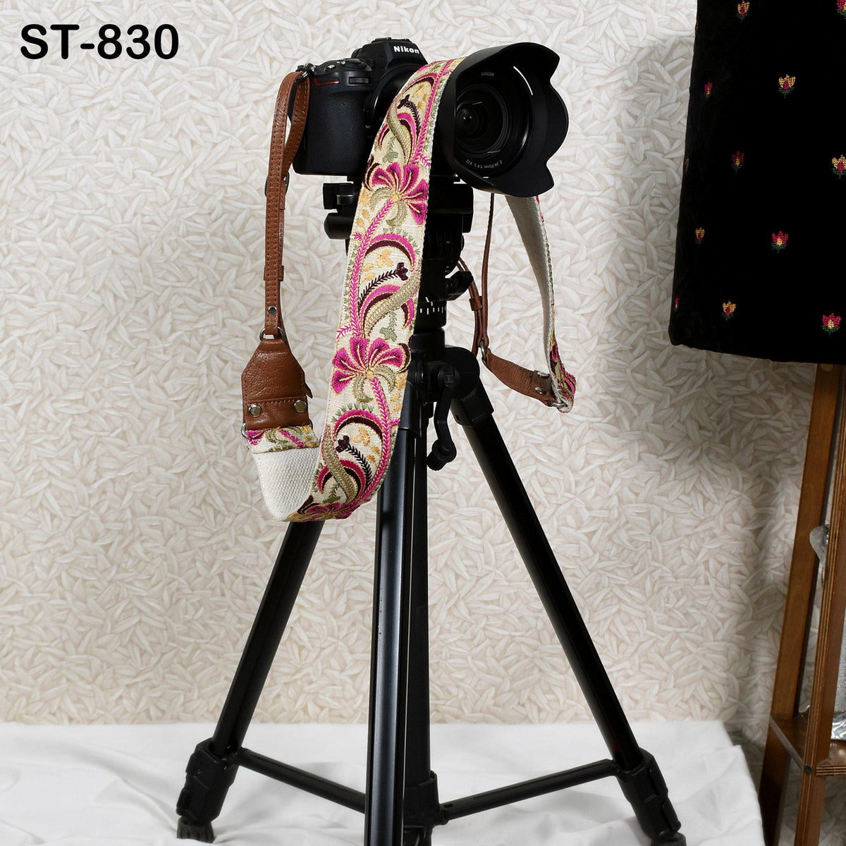 A camera mounted on a tripod with a colorful strap, placed against a patterned wall.
