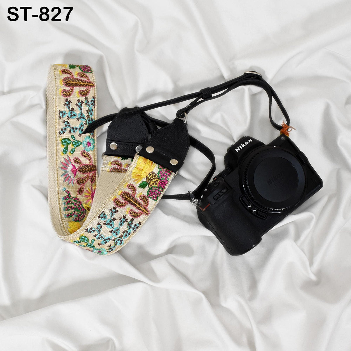 A floral patterned camera strap and a black camera are placed on a white fabric surface.