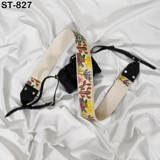 A camera strap with a colorful, embroidered pattern is draped over a white fabric surface.