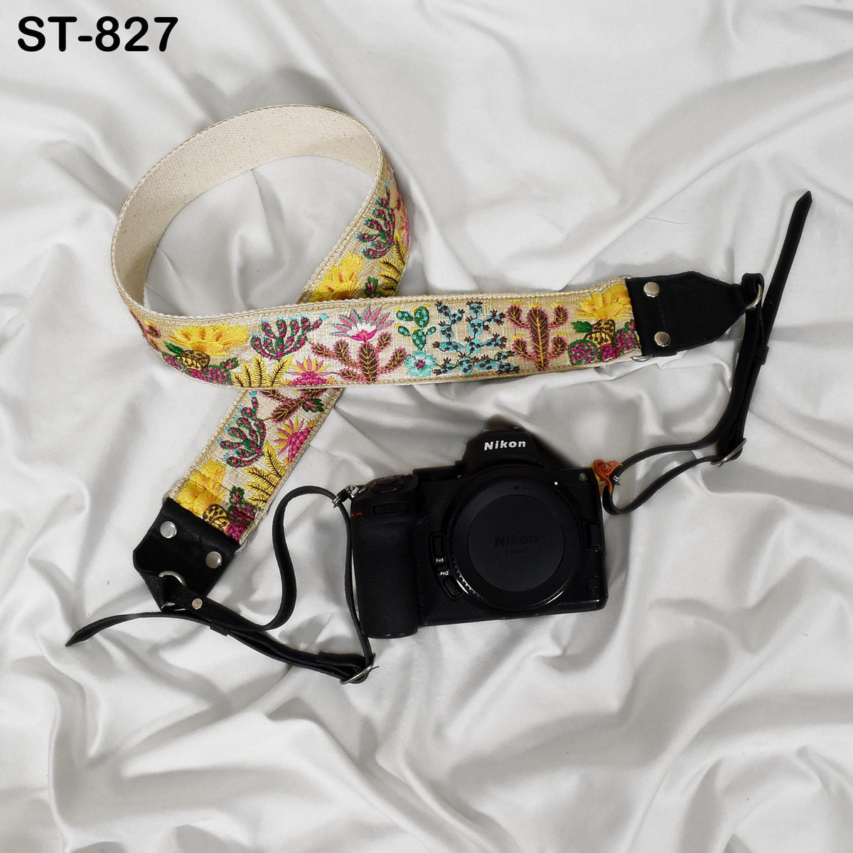 A floral patterned camera strap and a black Nikon camera are placed on a white fabric surface.