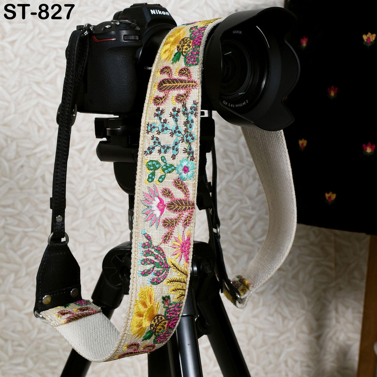 A black camera with a colorful, floral-patterned strap attached to it, placed on a tripod.