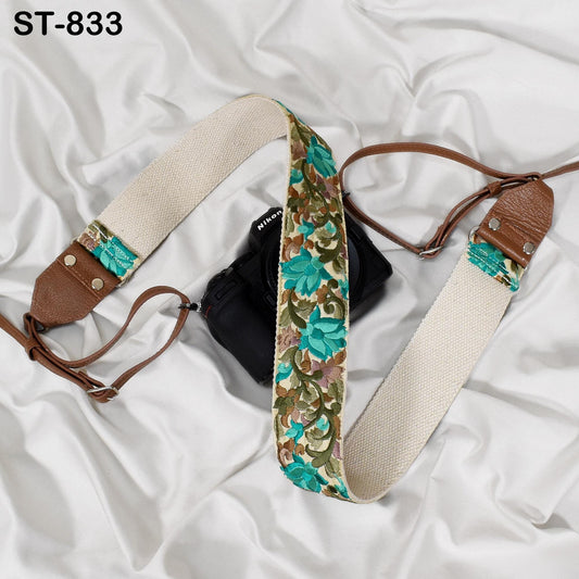 A floral patterned camera strap is draped over a black camera, with a white background.
