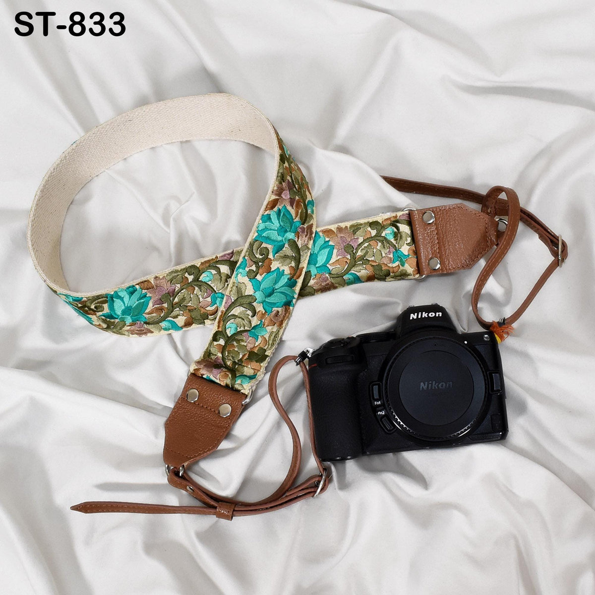 A floral patterned camera strap and a black Nikon camera are placed on a white fabric surface.