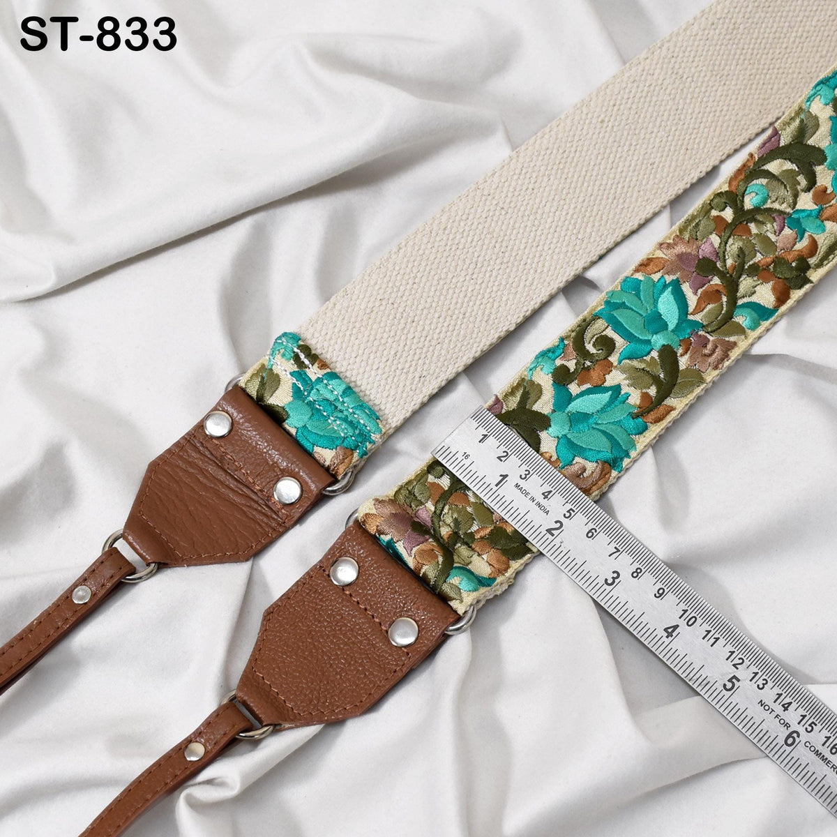 A brown leather strap with a floral pattern and a ruler placed on top of it, both resting on a white fabric background.