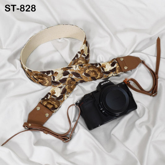 A floral-patterned camera strap and a black camera with a lens cap are placed on a white fabric surface.