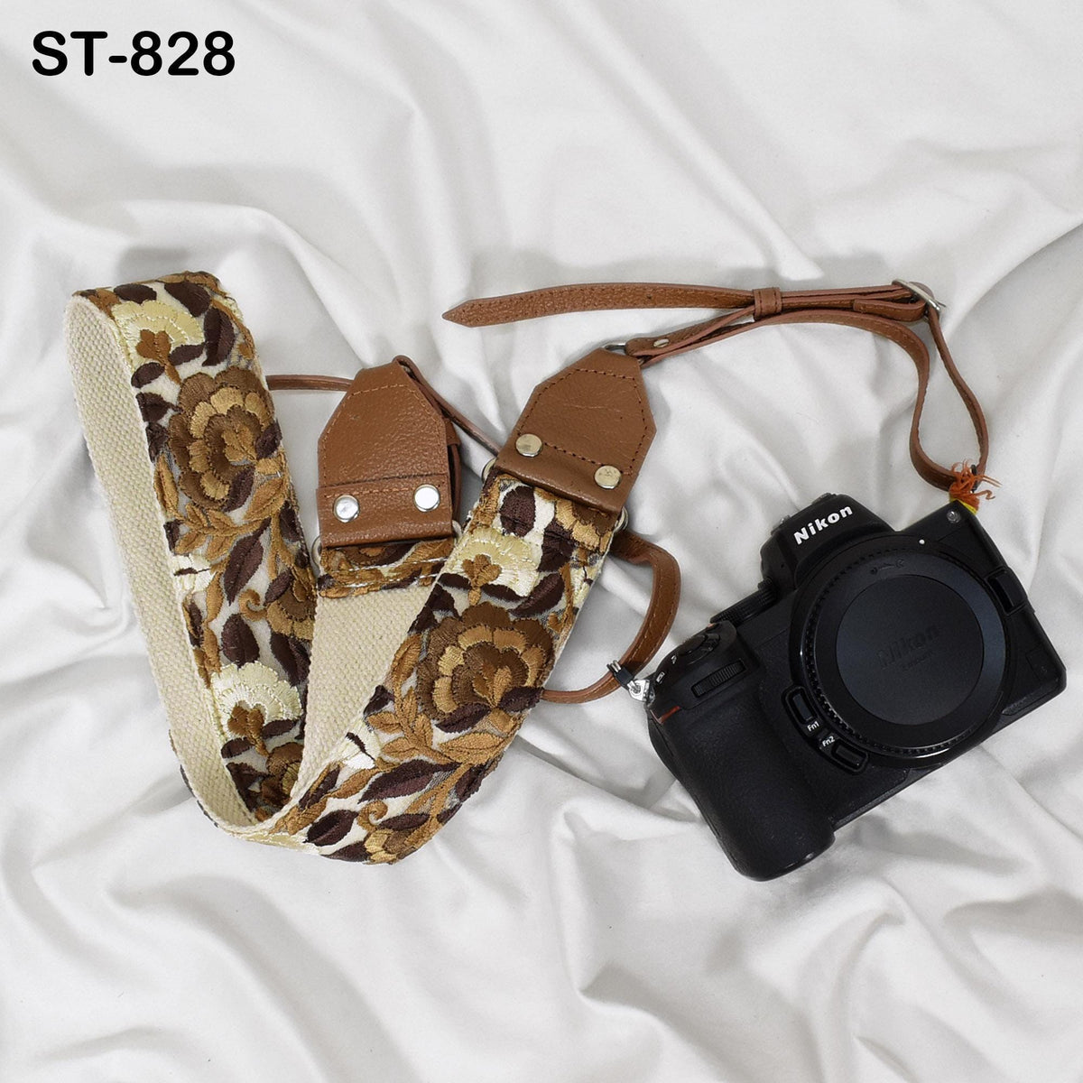 A floral patterned camera strap and a black Nikon camera are placed on a white fabric surface.