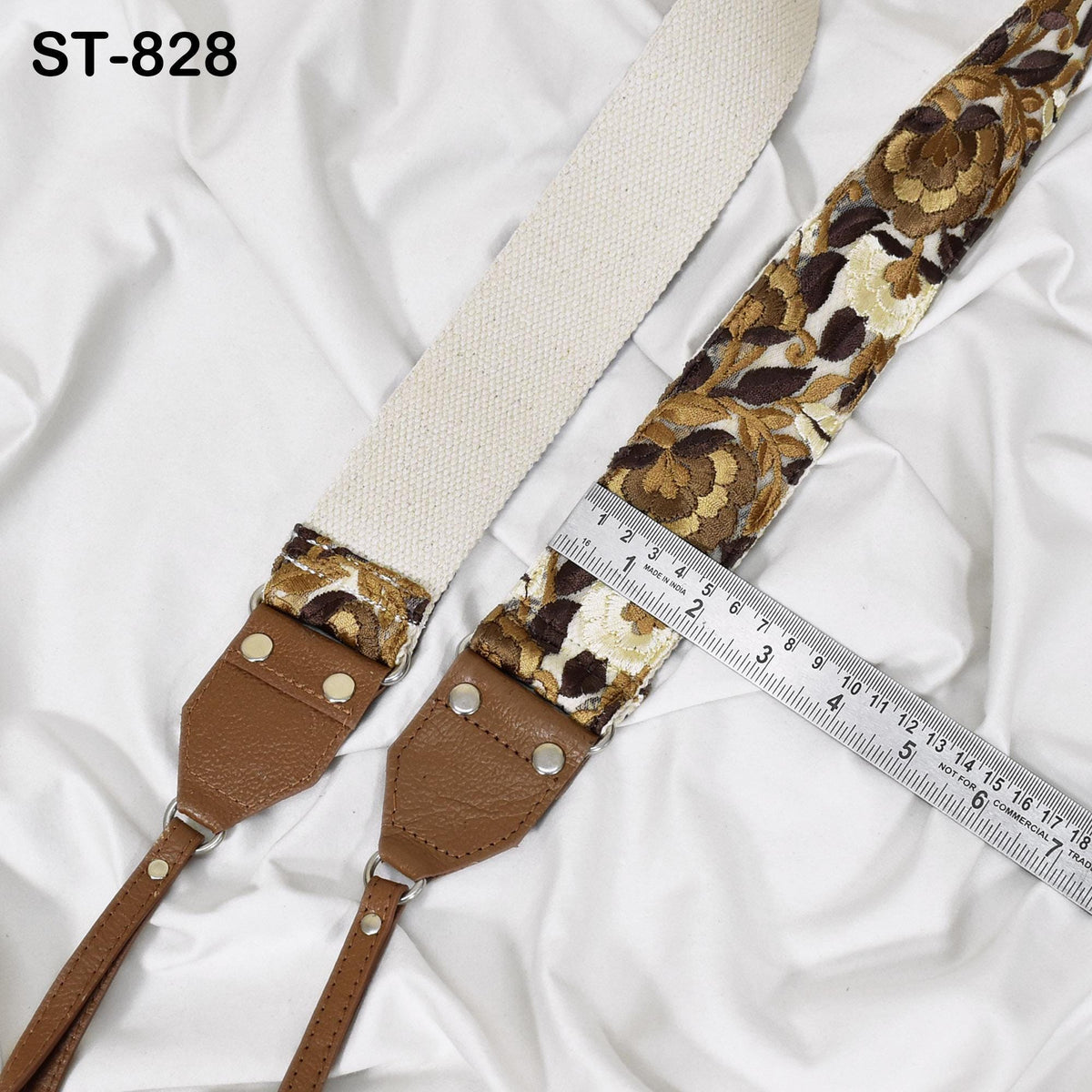 A brown and gold floral patterned strap with a white strap attached, placed on a white fabric surface. A ruler is visible next to the strap, indicating the strap's length.