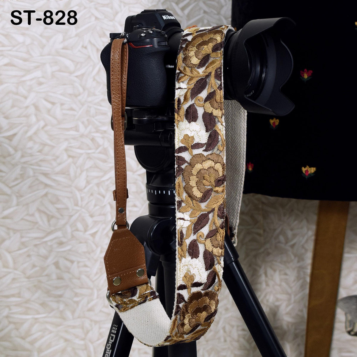 A camera strap with a floral pattern is hanging on a tripod, with a camera attached to the top of the tripod.