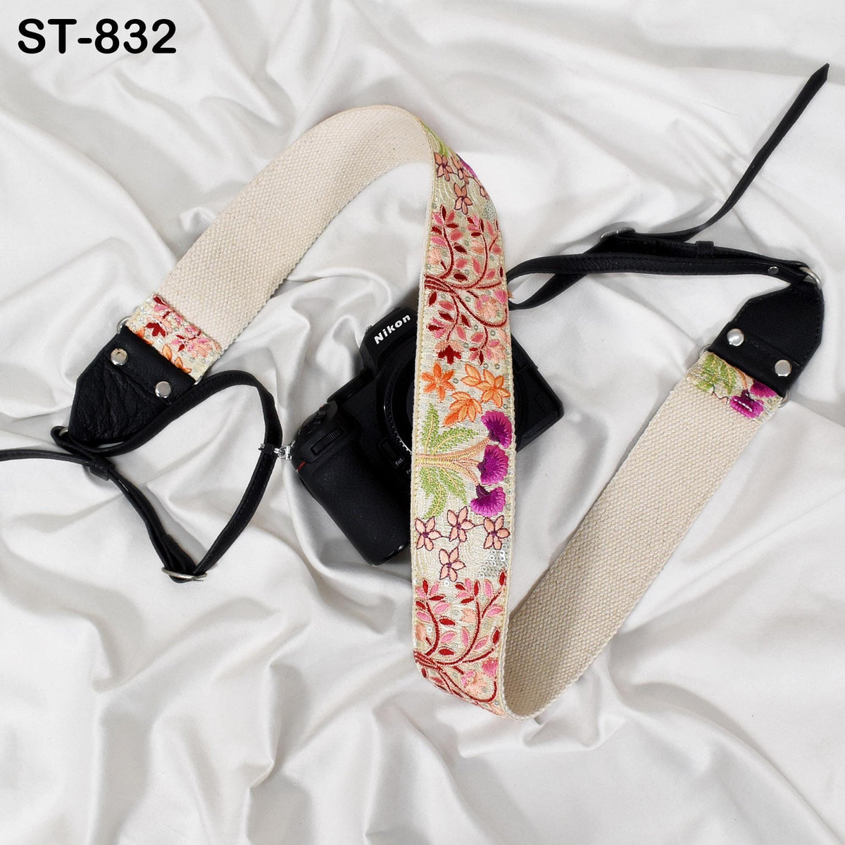 A camera strap with a floral pattern and a black camera body are placed on a white surface.