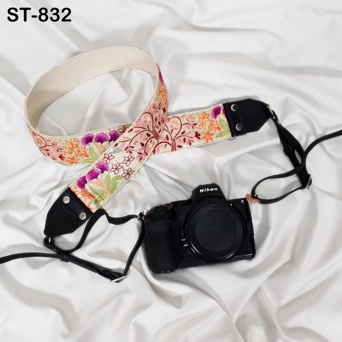 A floral patterned camera strap and a black Nikon camera are placed on a white, crumpled surface.