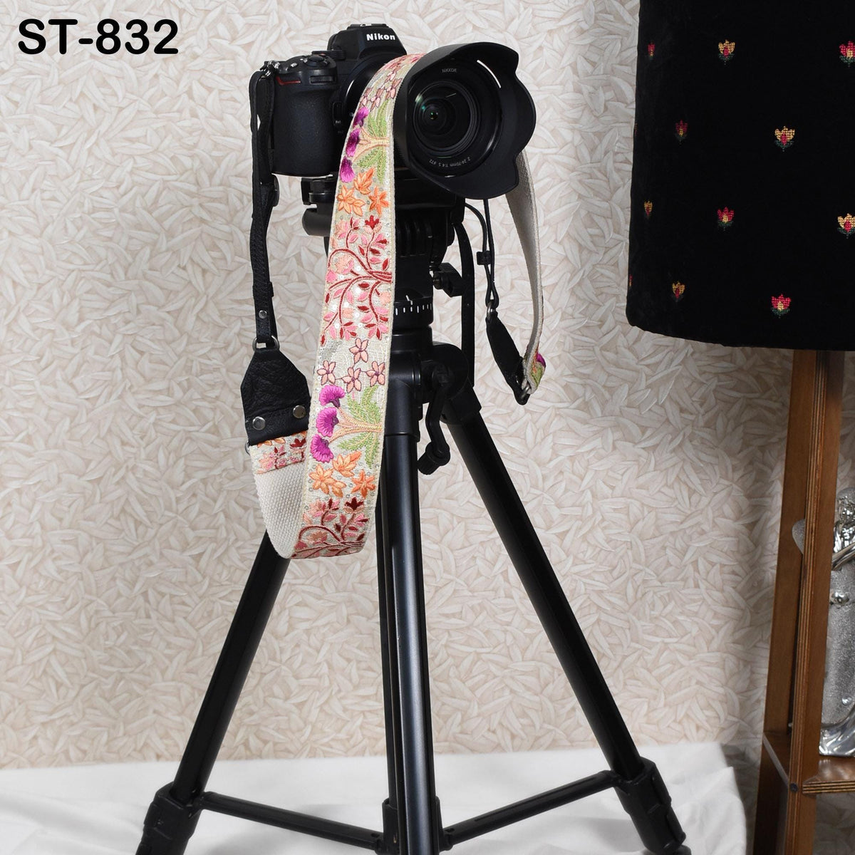 A black tripod with a camera mounted on top, along with a colorful strap, is placed against a patterned wall.