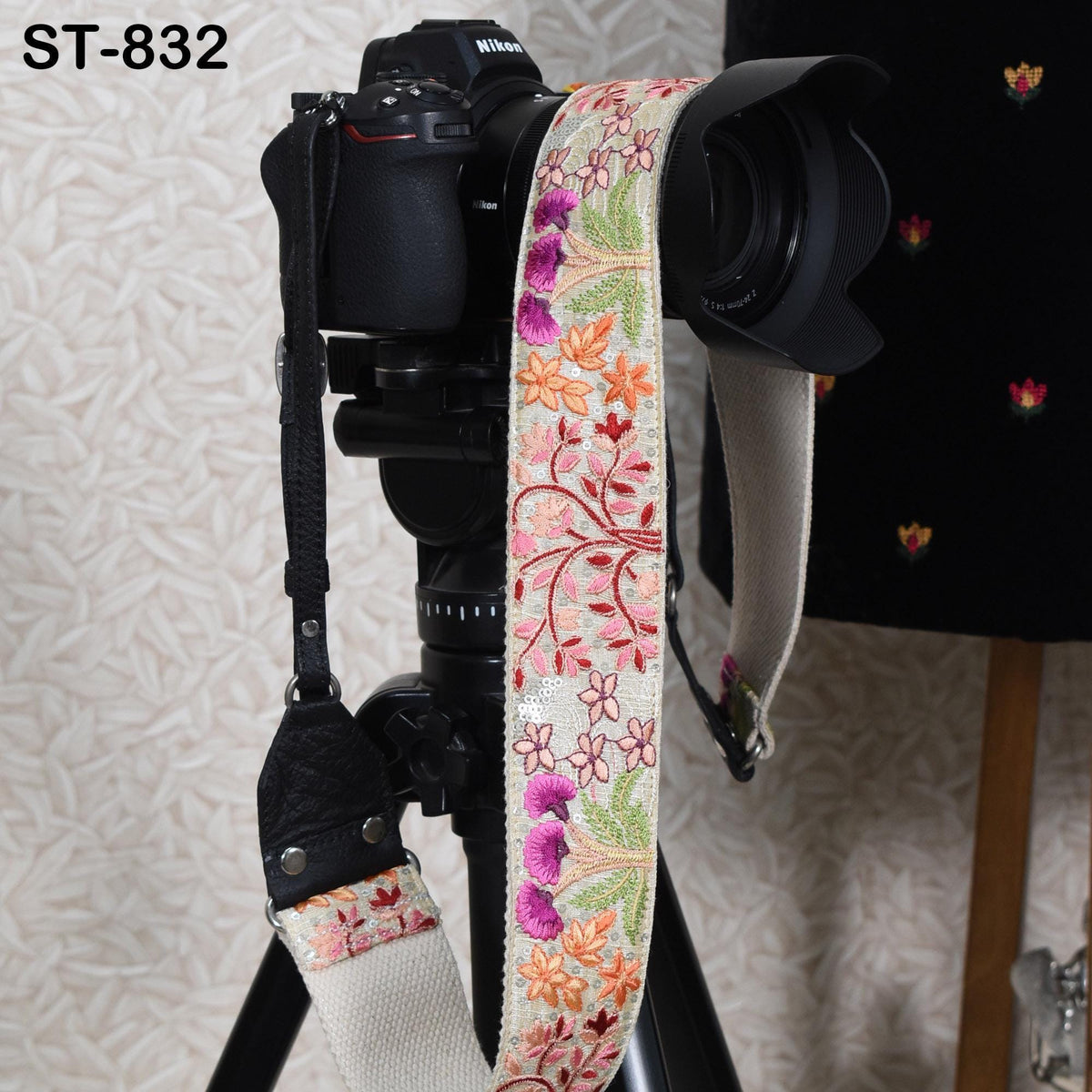 A black camera with a colorful floral strap attached to it, placed on a tripod.