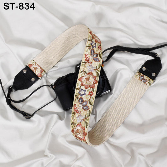 A camera strap with a floral pattern is placed on a white fabric surface.