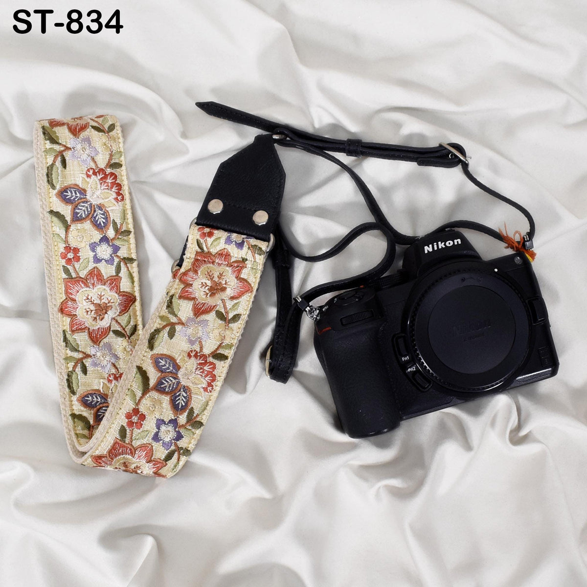 A floral patterned camera strap and a Nikon camera are placed on a white fabric surface.