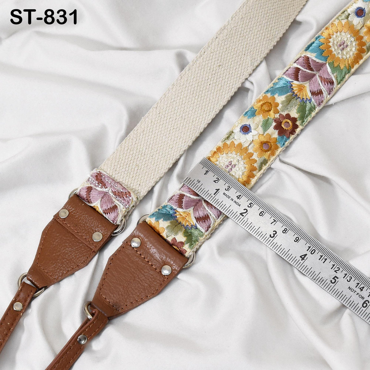a beige and floral patterned strap with a leather buckle, placed on a white fabric surface. A ruler is visible, likely used for measuring the strap's length.