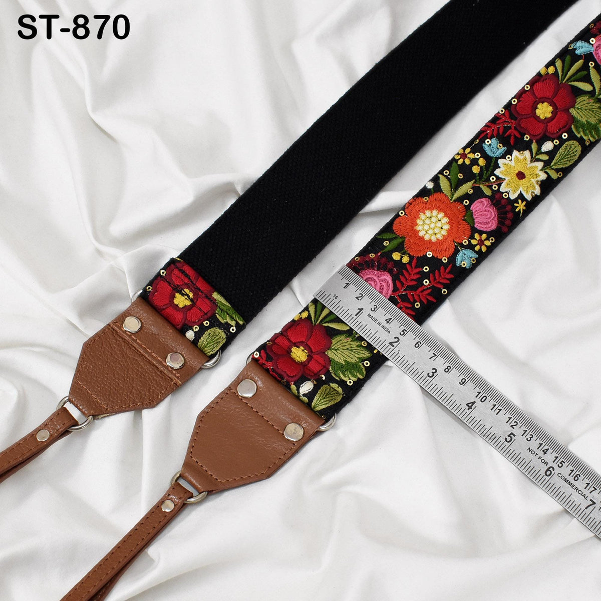 A black strap with a floral pattern and a brown leather strap are placed on a white fabric surface, with a ruler placed next to them.