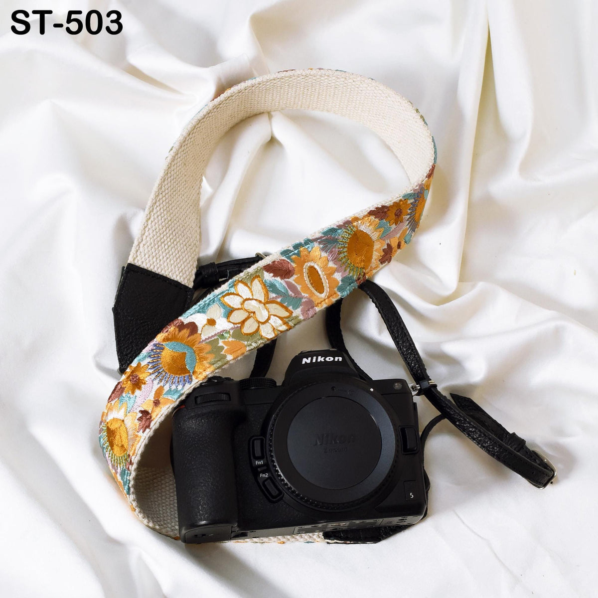 A black camera with a colorful floral strap is placed on a white surface.